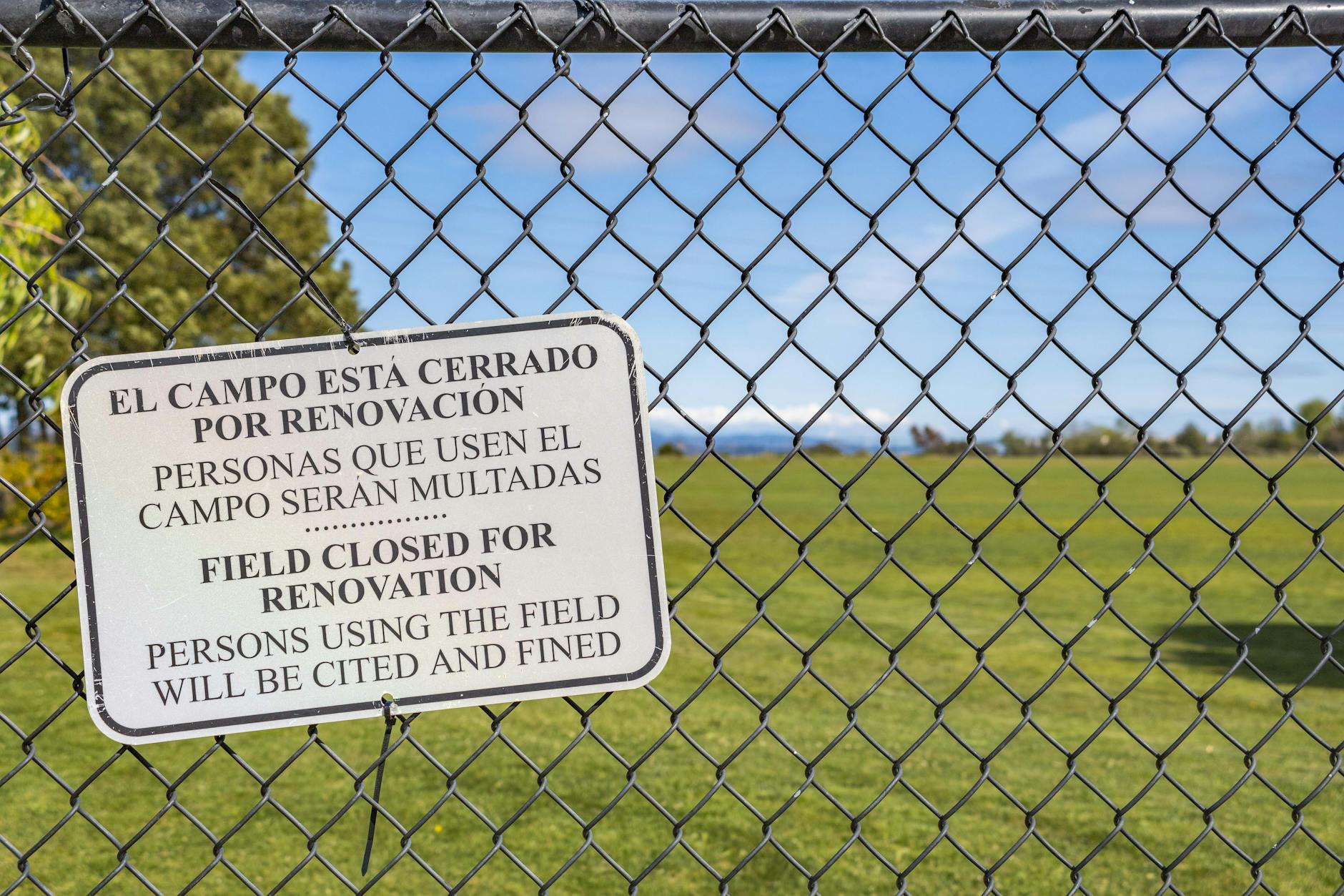 A field closed sign on a chain link fence indicating restricted access to the grassy area.