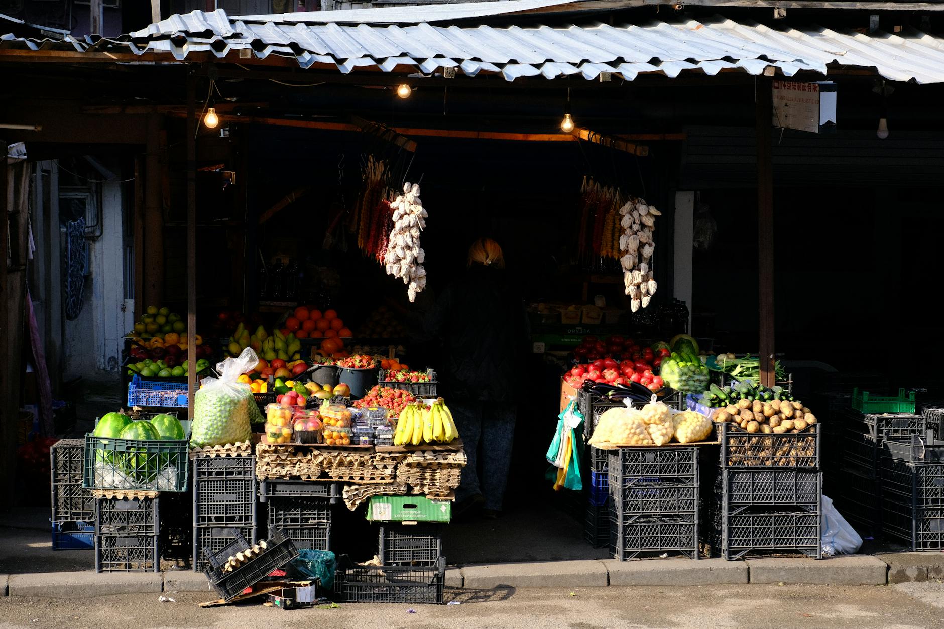 Colorful outdoor market stall in Georgia displaying fresh fruits and vegetables under a rustic roof.