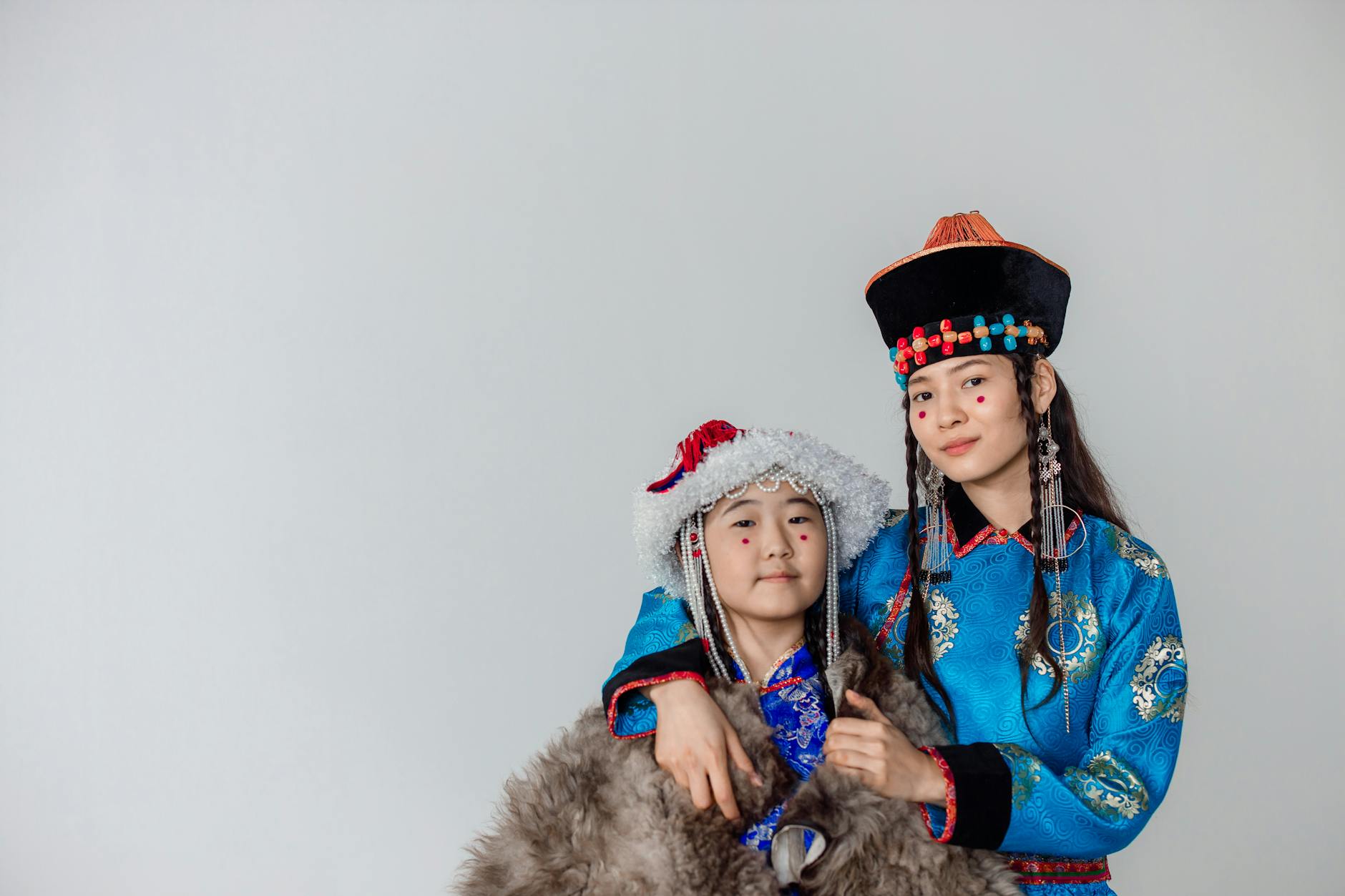 Two people in traditional Mongolian clothing, embracing in a studio setting. White background.