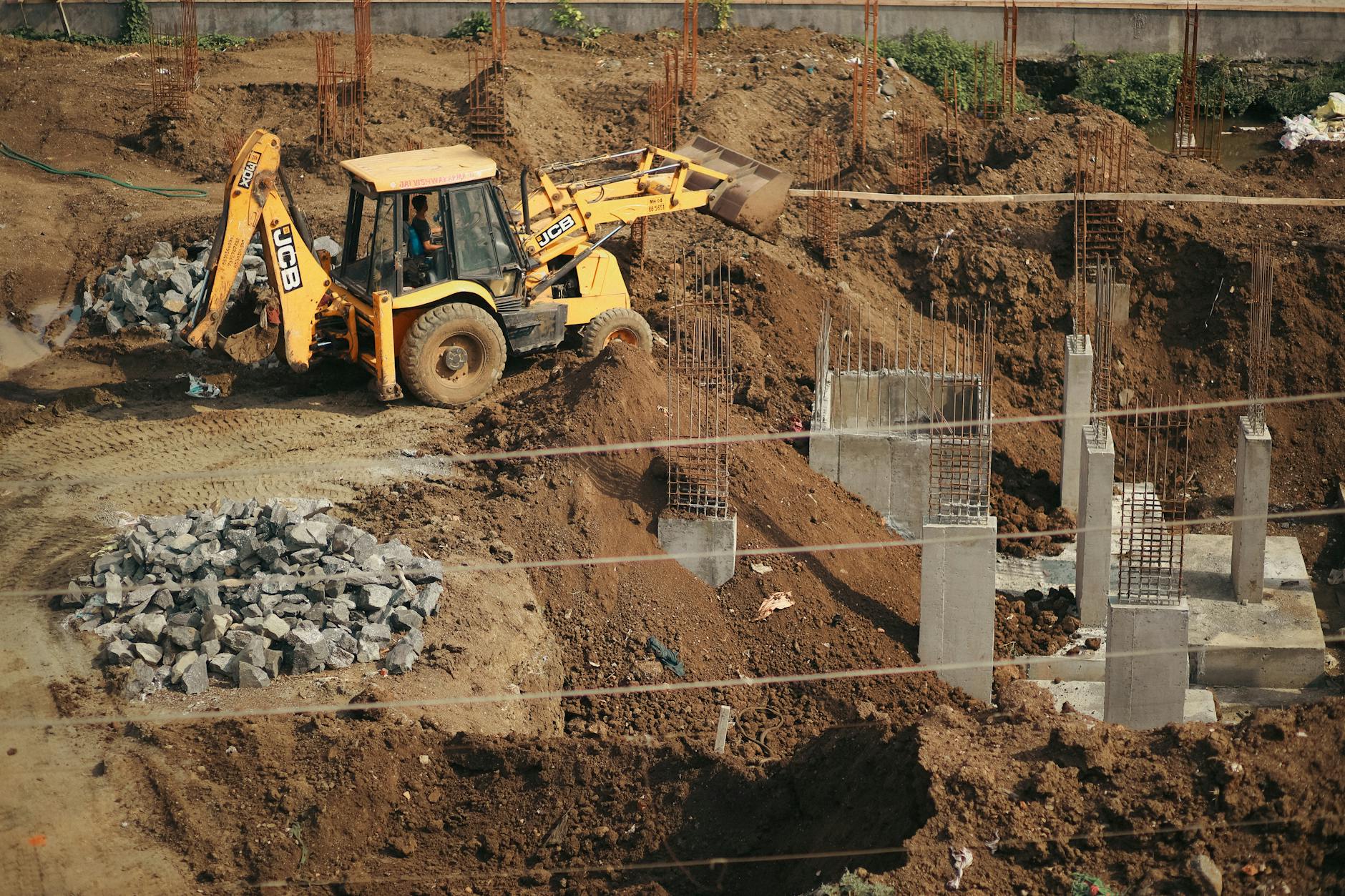 A bulldozer moves soil at a busy construction site, surrounded by piles of gravel and concrete structures.
