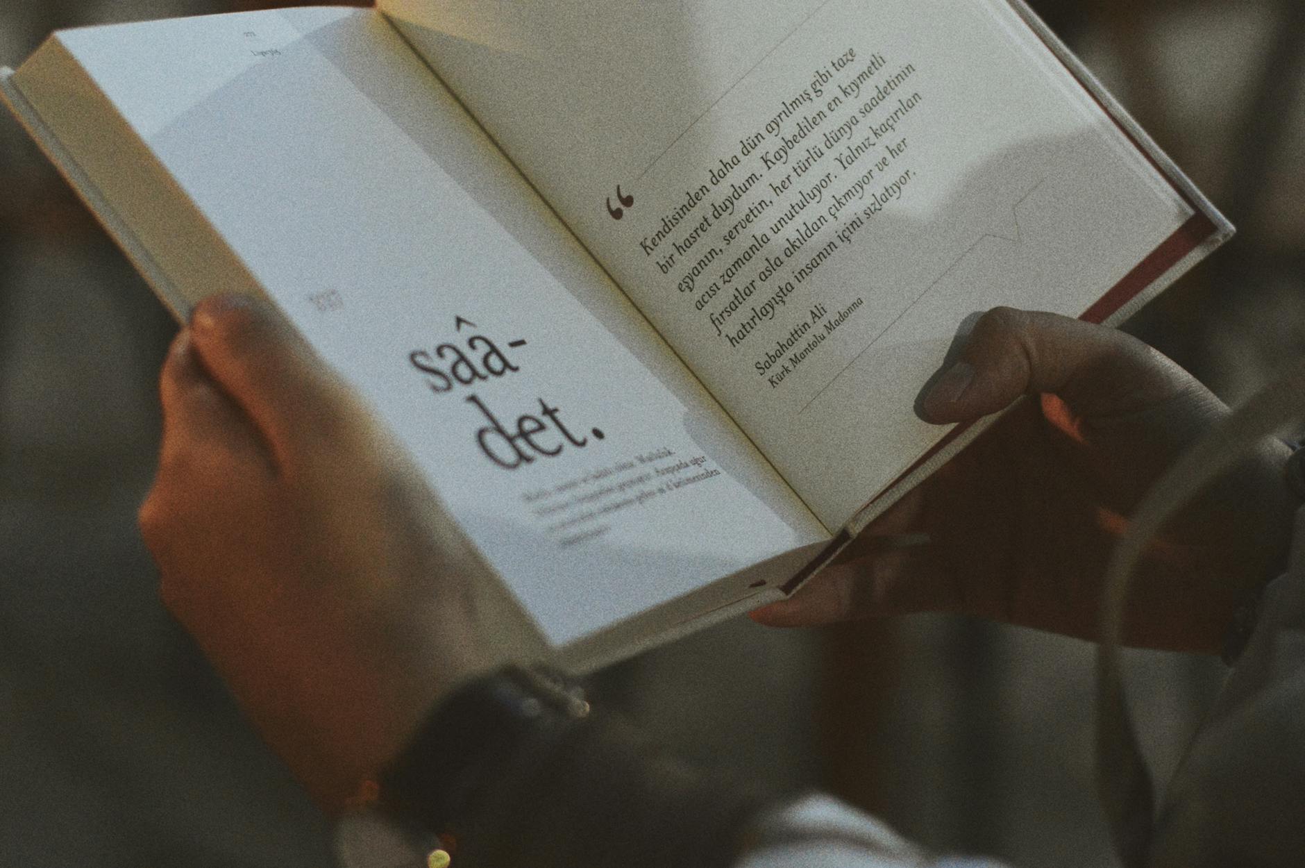 Person holding and reading an open book with visible text.