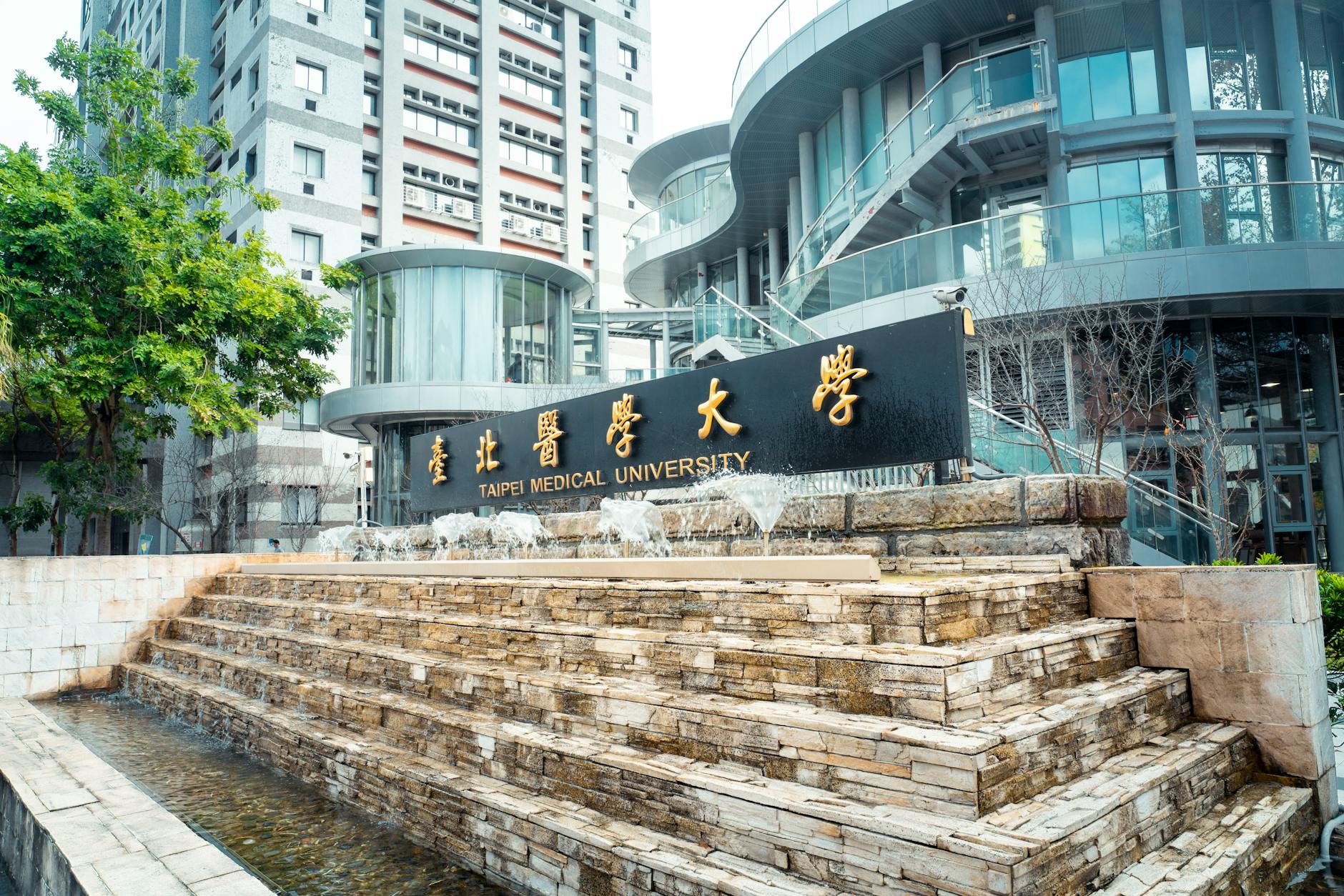 Modern architectural view of Taipei Medical University with fountain feature outdoors.