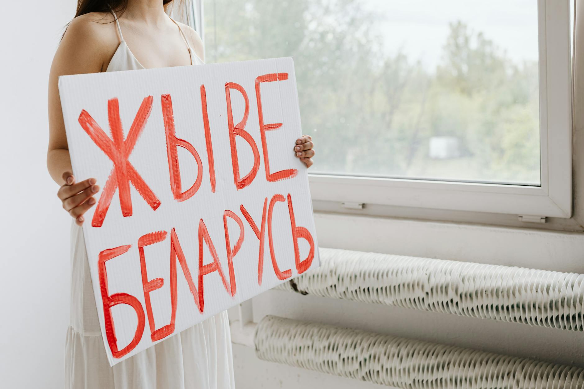 A woman holds a Belarusian sign near a window, symbolizing activism.