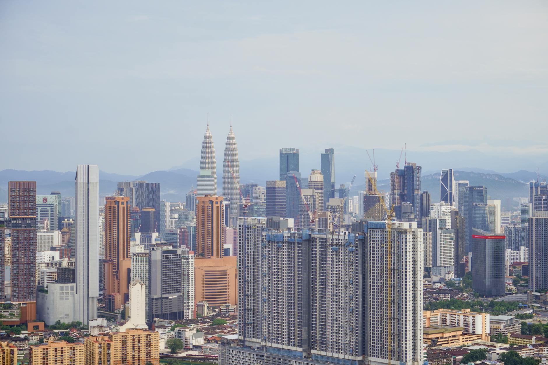 Aerial view of Kuala Lumpur's skyline with iconic Petronas Towers under a clear blue sky.